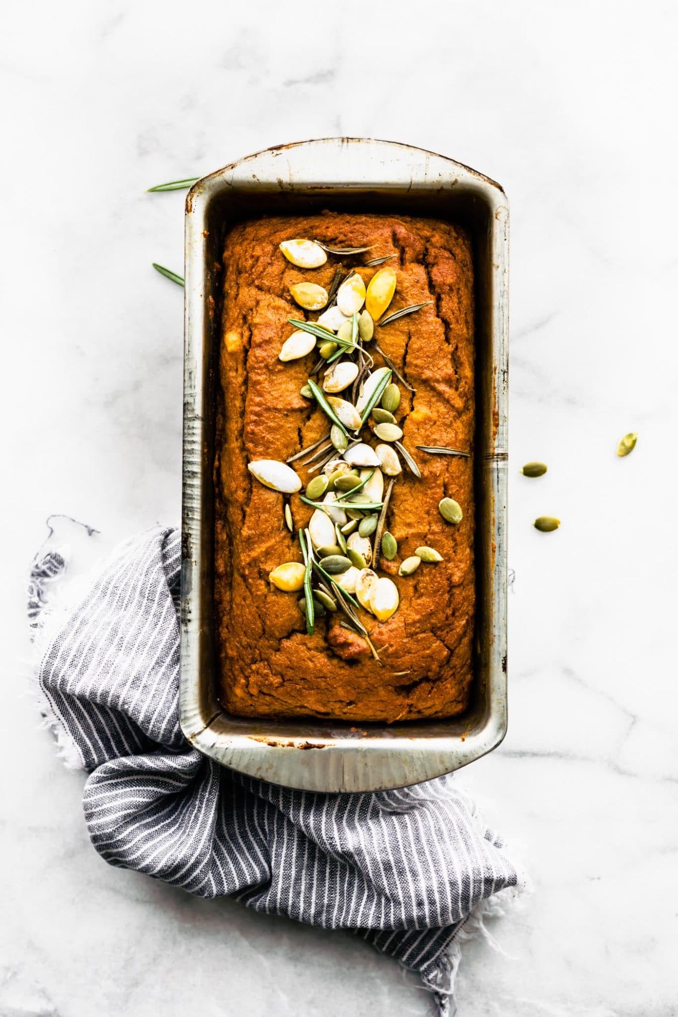 A loaf of pumpkin bread with rosemary and pumpkin seeds sprinkled on top