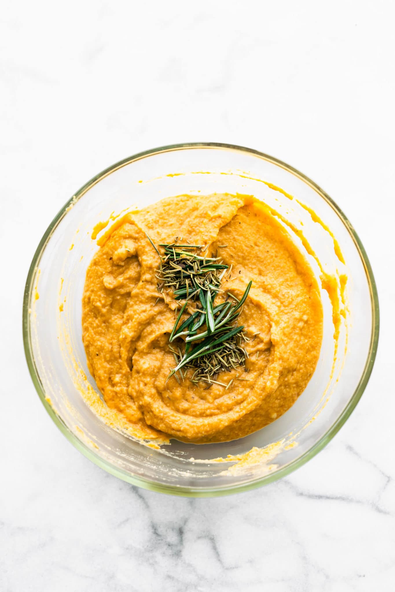 pumpkin bread dough in a clear bowl topped with fresh rosemary