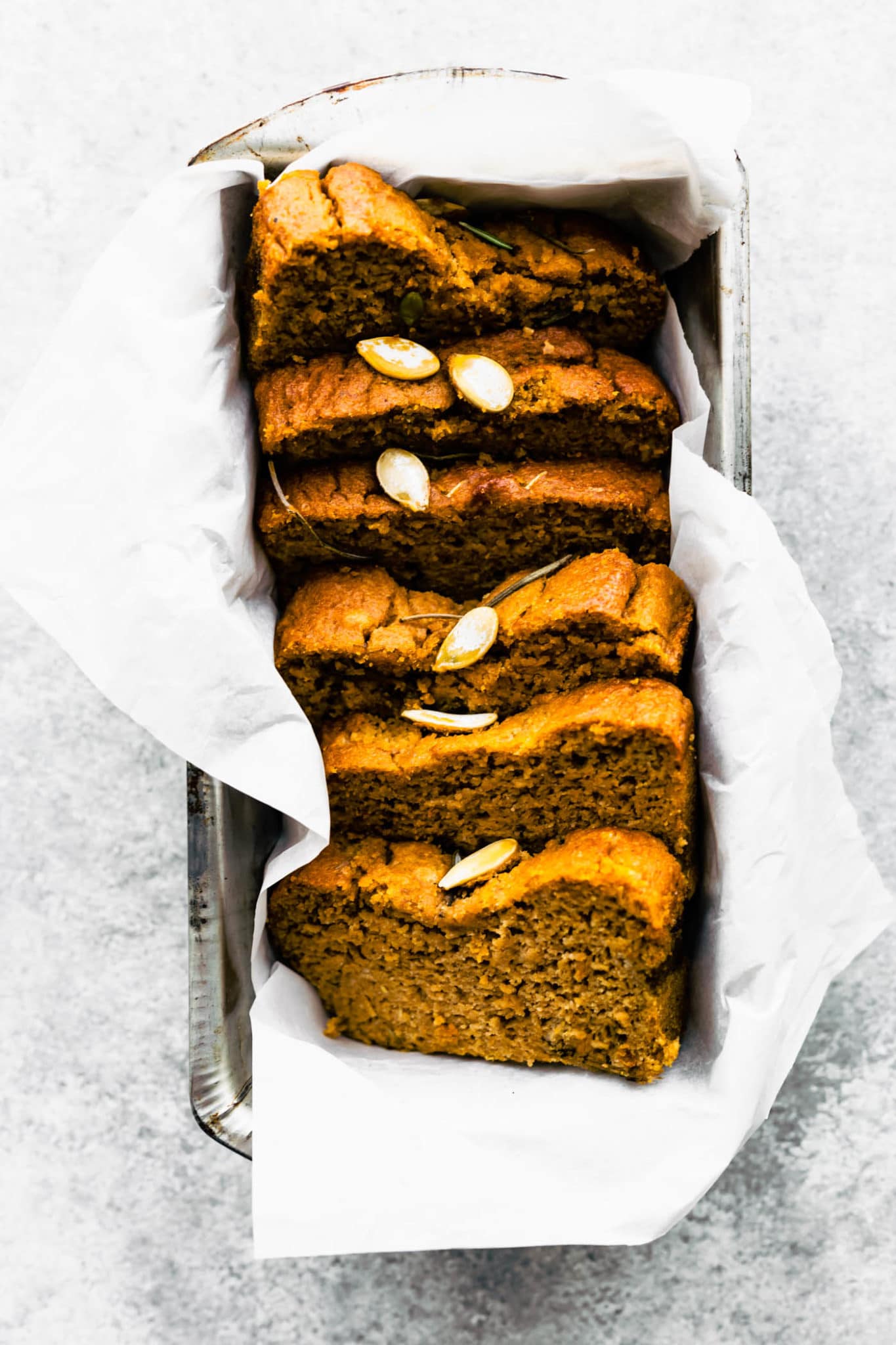 A loaf of pumpkin bread with rosemary cut into thick slices placed in parchment-lined loaf pan.