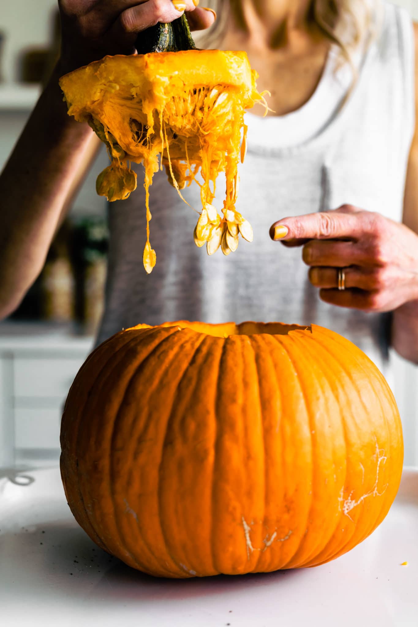 Woman holding the top of a pumpkin with seeds dangling down pointing to the seeds