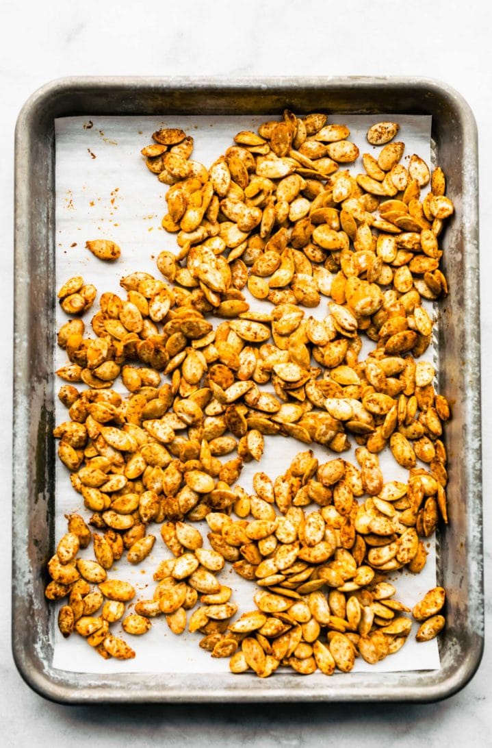 Roasted pumpkin seeds with seasoning on parchment-lined baking sheet.