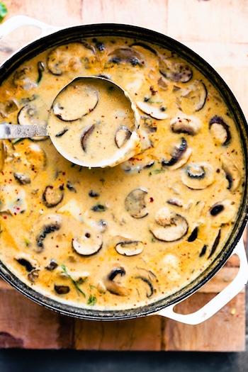 ladle of mushroom soup in pan on wood backdrop.