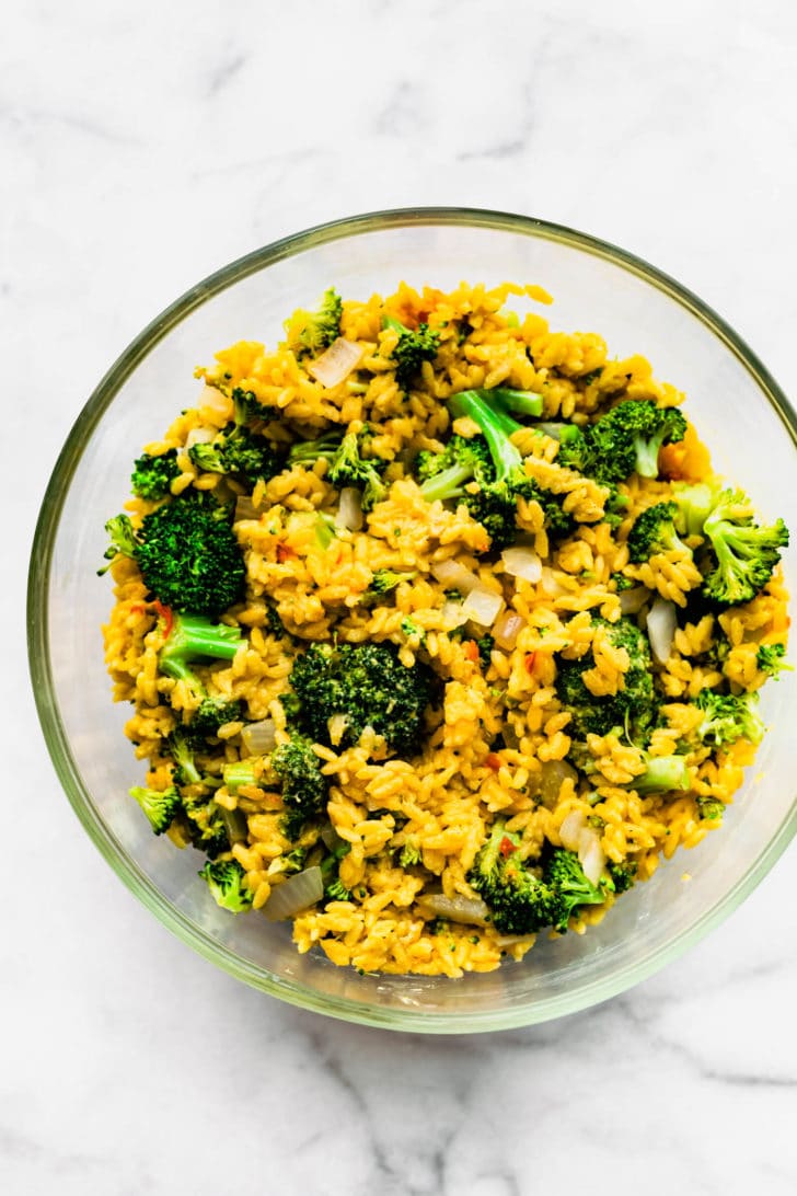 Overhead view mixture of broccoli cheese orzo in clear glass bowl.
