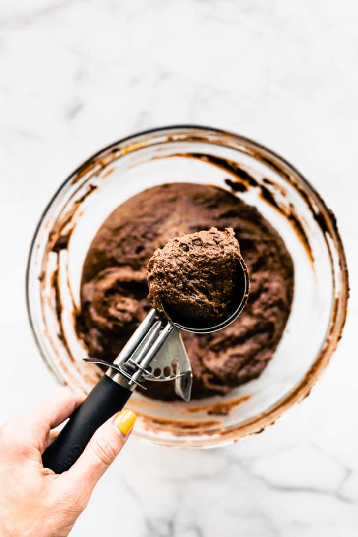 Overhead view of a scoop holding the batter of gluten free chocolate cupcakes over a bowl of batter.