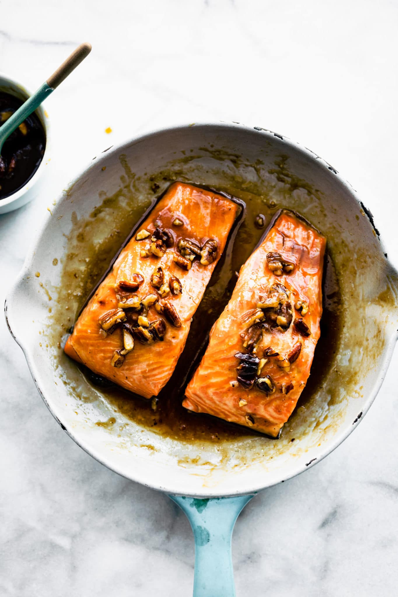 Two pieces of salmon marinading in a maple bourbon glaze with nuts in a saucepan.