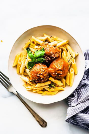 overhead photos of plantbased meatballs in pasta with red sauce in white bowl. fork on side.