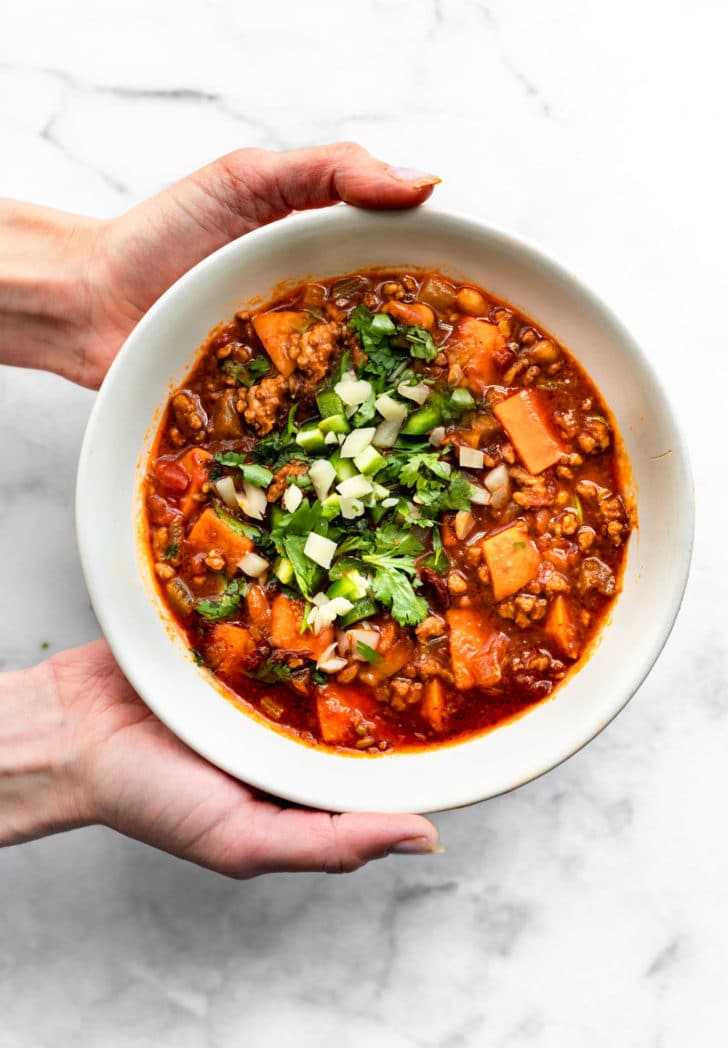 two hands holding a bowl of sweet potato turkey chili