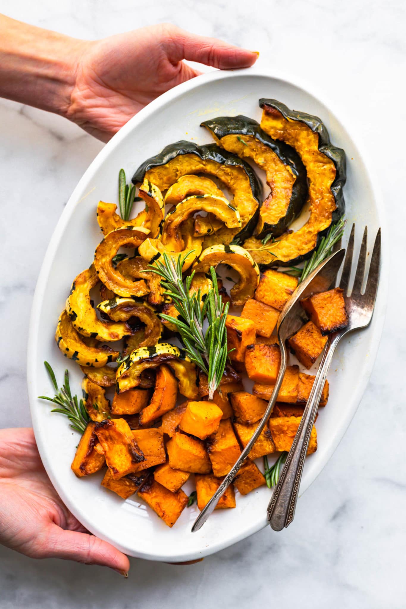 roasted air fryer squash on a white serving platter with a spoon, fork, and fresh herbs