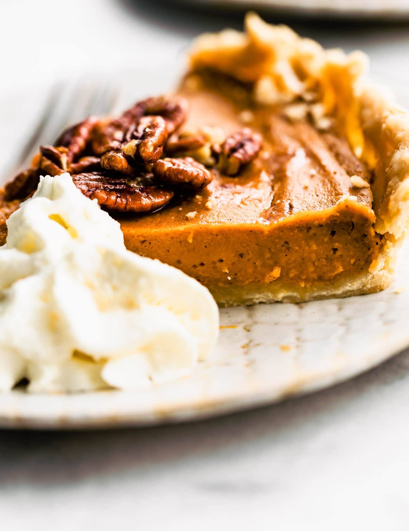 slice of vegan gluten free pumpkin pie on a white plate with coconut cream on the side