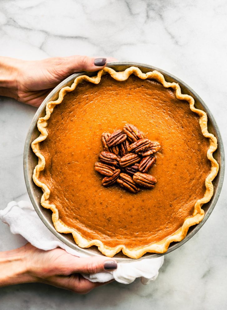 Two hands holding a gluten free pumpkin pie topped with pecans.