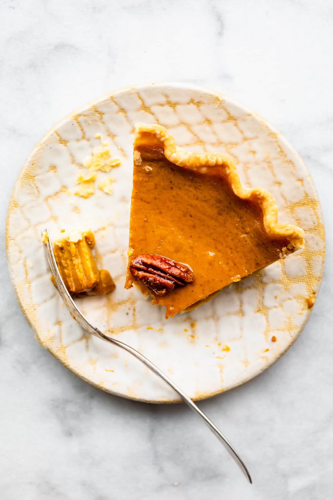 overhead view of gluten free pumpkin pie with a bite taken out plated on a white and yellow plate.