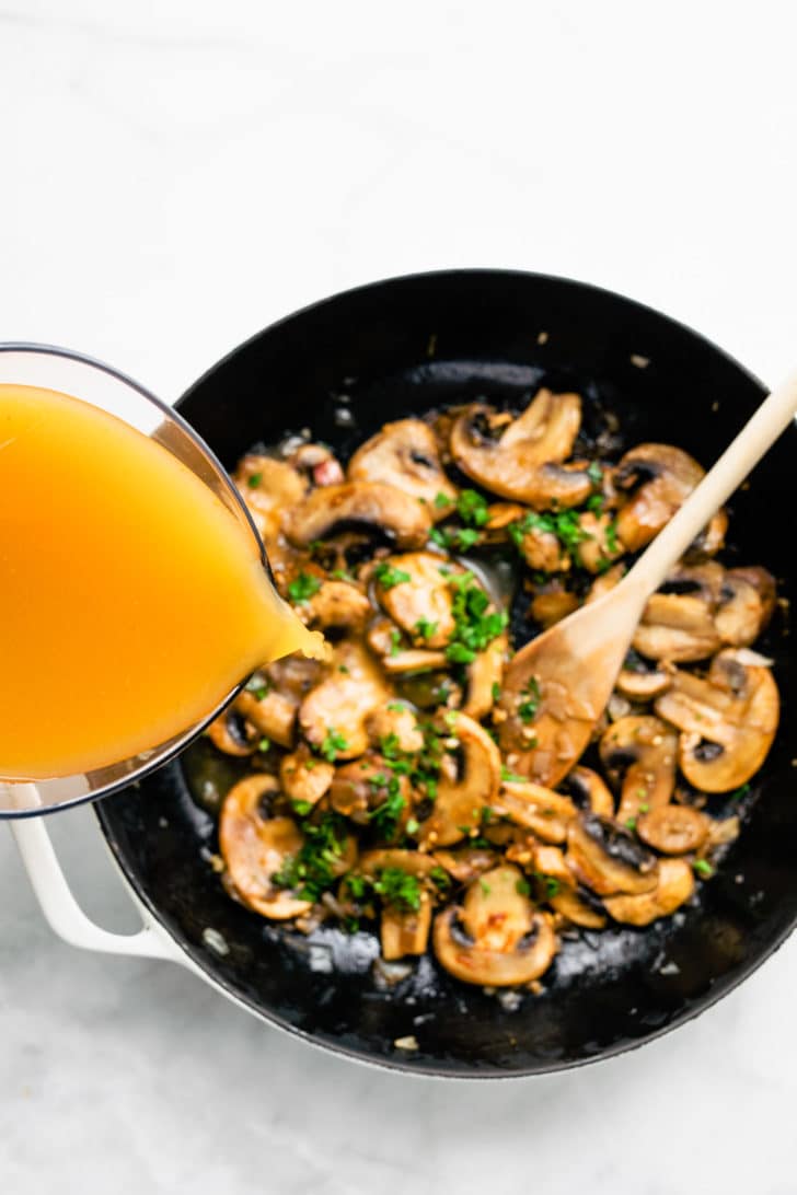 broth being poured on top of mushrooms and herbs to create gluten free vegan mushroom gravy