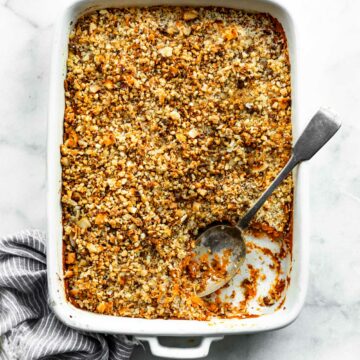 White casserole dish filled with vegan sweet potato casserole with a corner missing and a serving spoon