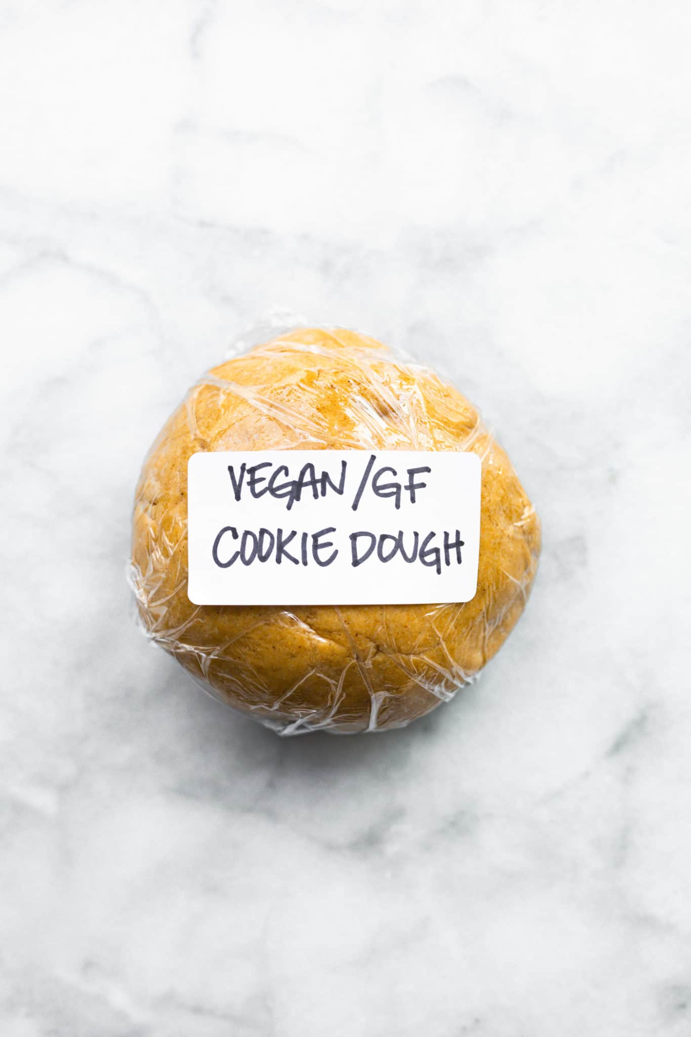 Vegan and gluten free cookie dough rolled into a ball and wrapped with cling wrap