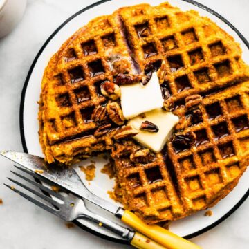 Gluten free sweet potato waffle with a bite taken out topped with butter on a plate with a knife and fork