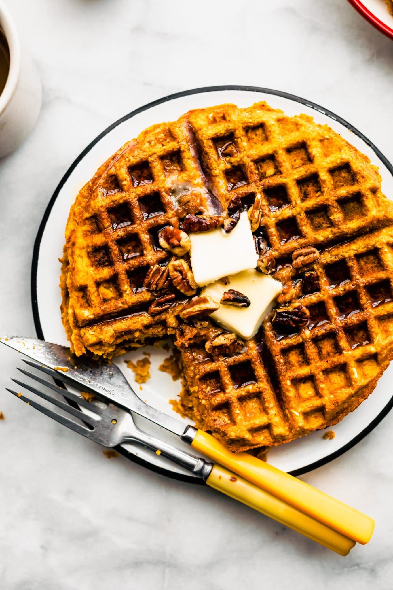 Gluten free sweet potato waffle with a bite taken out topped with butter on a plate with a knife and fork