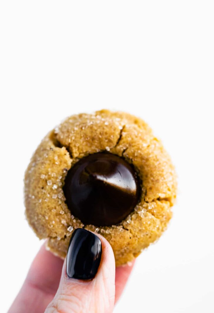 A gluten free sugar cookie mix made into a peanut butter kiss cookie, being held between thumb and forefinger.
