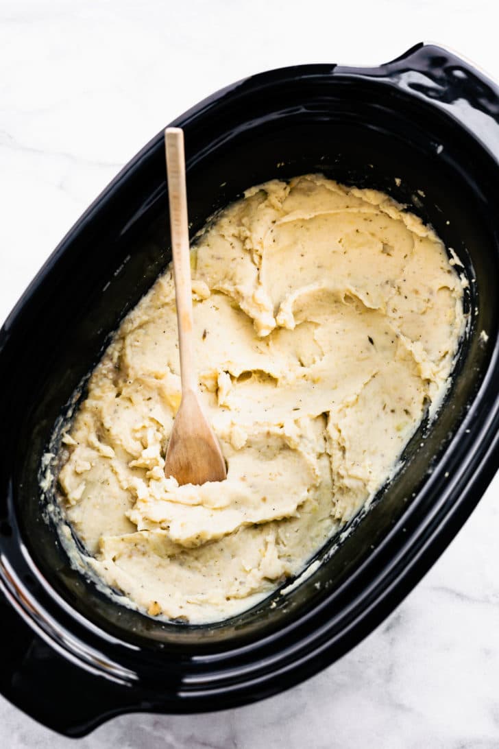creamy dairy free mashed potatoes in a slow cooker being stirred with a wooden spoon