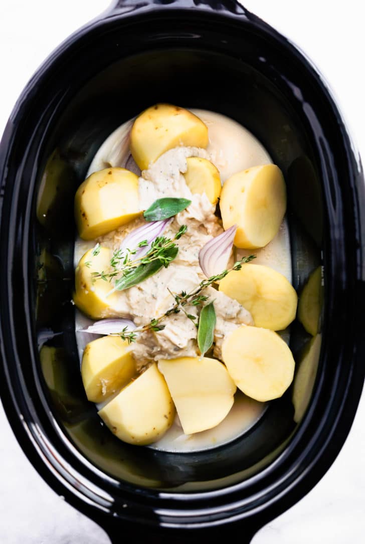 Sliced potatoes, dairy free milk, shallots, fresh herbs, and white bean puree in a slow cooker for dairy free mashed potatoes