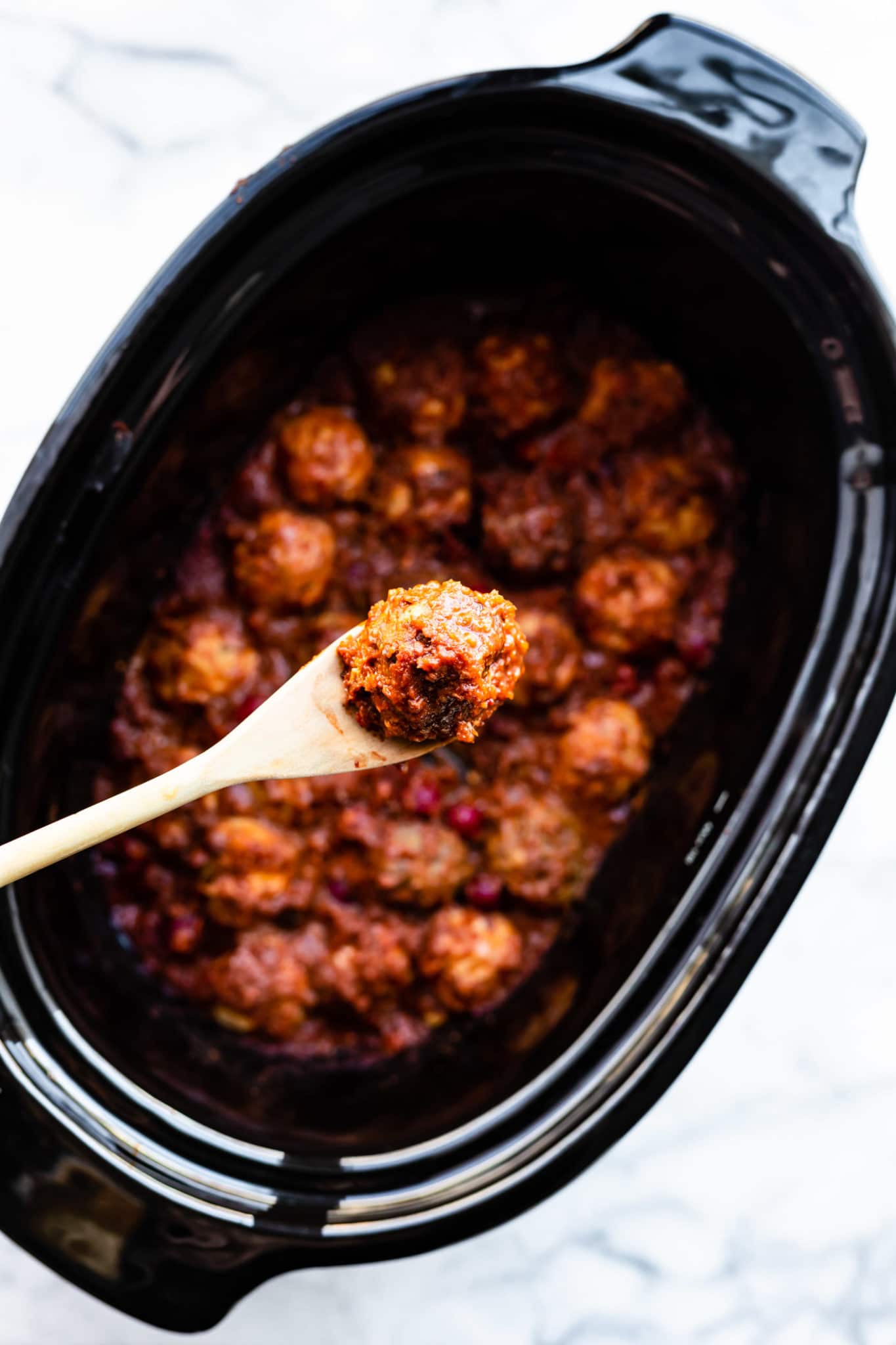 a wooden spoon holding a gluten free meatball over a slow cooker of meatballs