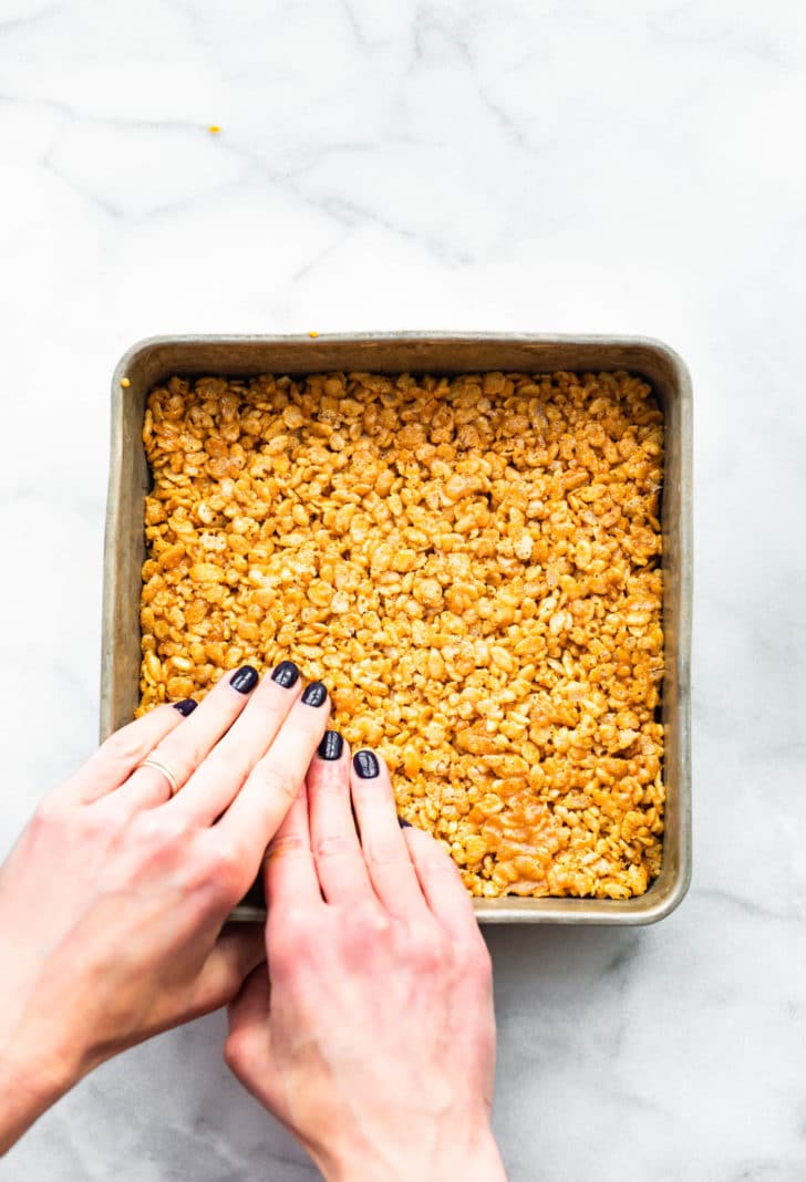 two hands pressing vegan peanut butter rice krispie treats into a baking pan