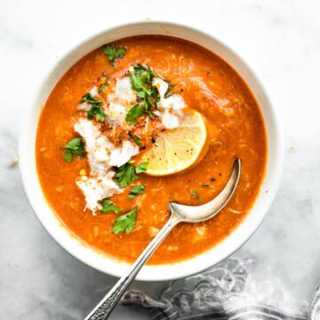 a bowl of tomato crab bisque topped with lemon and herbs with a spoon sticking out