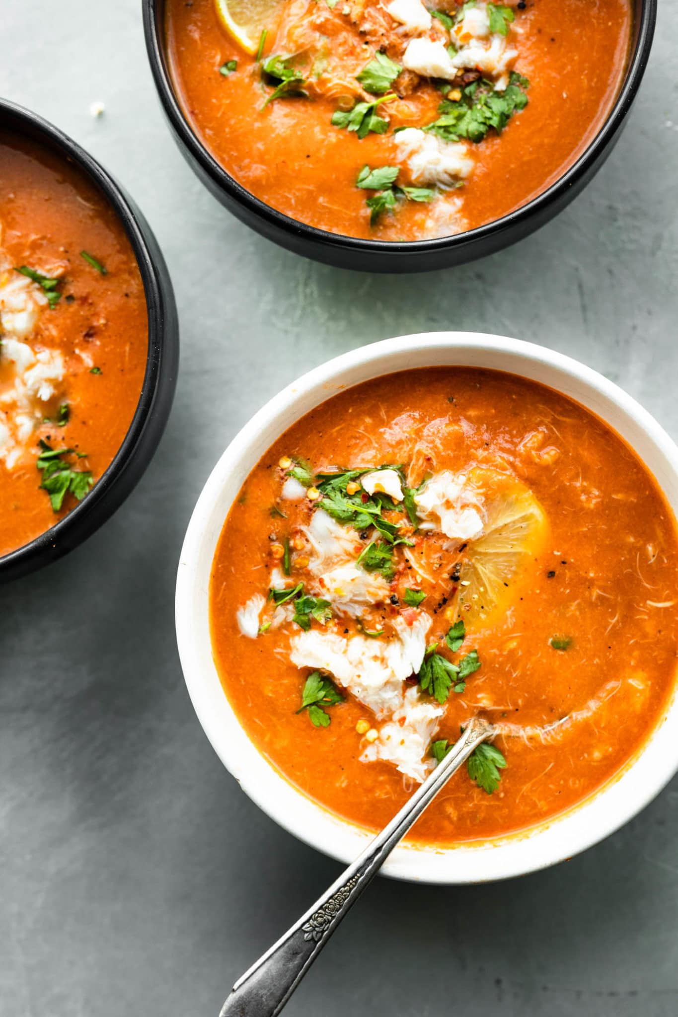 three bowls of tomato crab bisque topped with fresh herbs and lemon slices