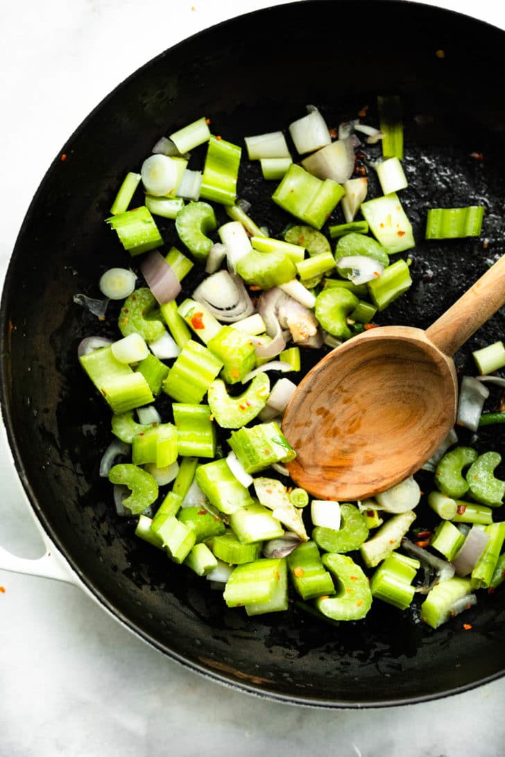celery and onions being sauteed with a wooden spoon for tomato crab bisque