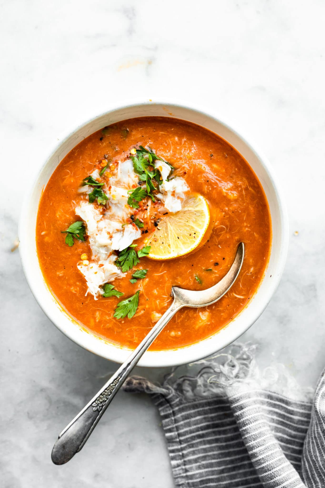 a bowl of tomato crab bisque topped with lemon and herbs with a spoon sticking out