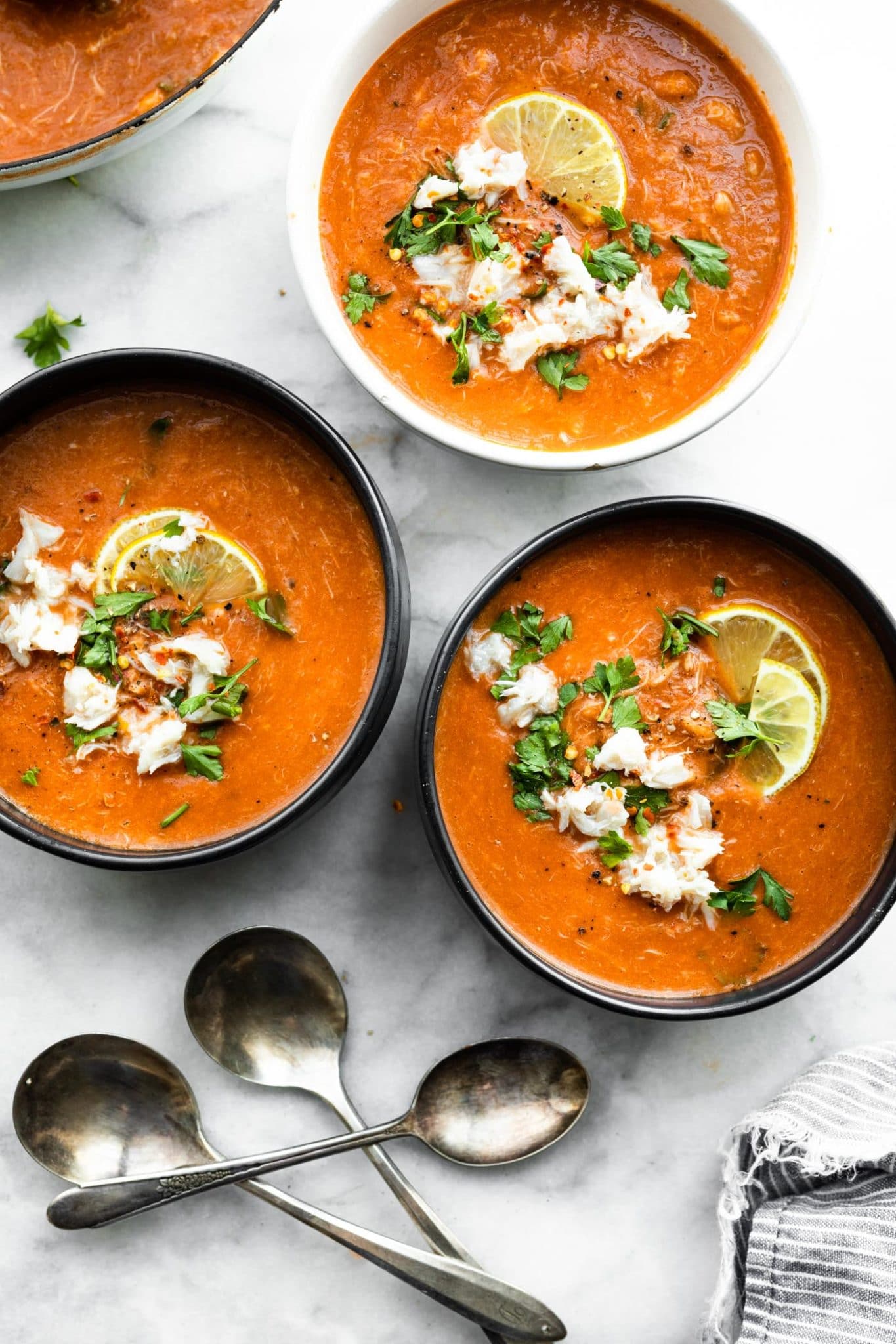 three bowls of tomato crab bisque topped iwth lemon slices and fresh herbs