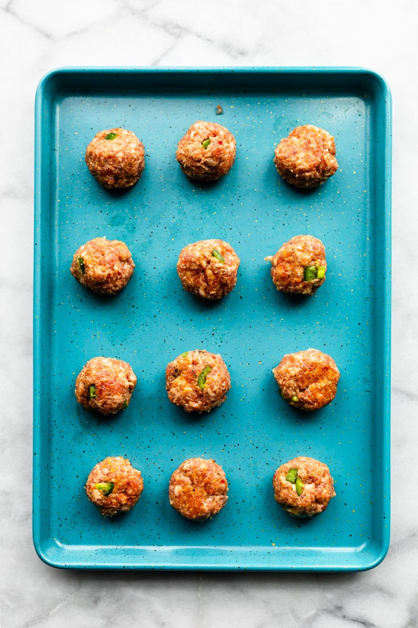 gluten free meatballs lined up on turquoise baking sheet ready to be baked.