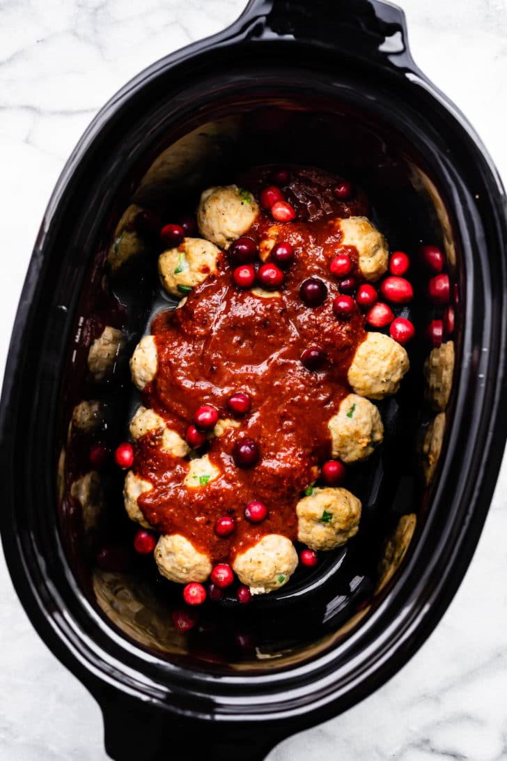 gluten free meatballs in a slow cooker topped with a cranberry sauce and cranberries