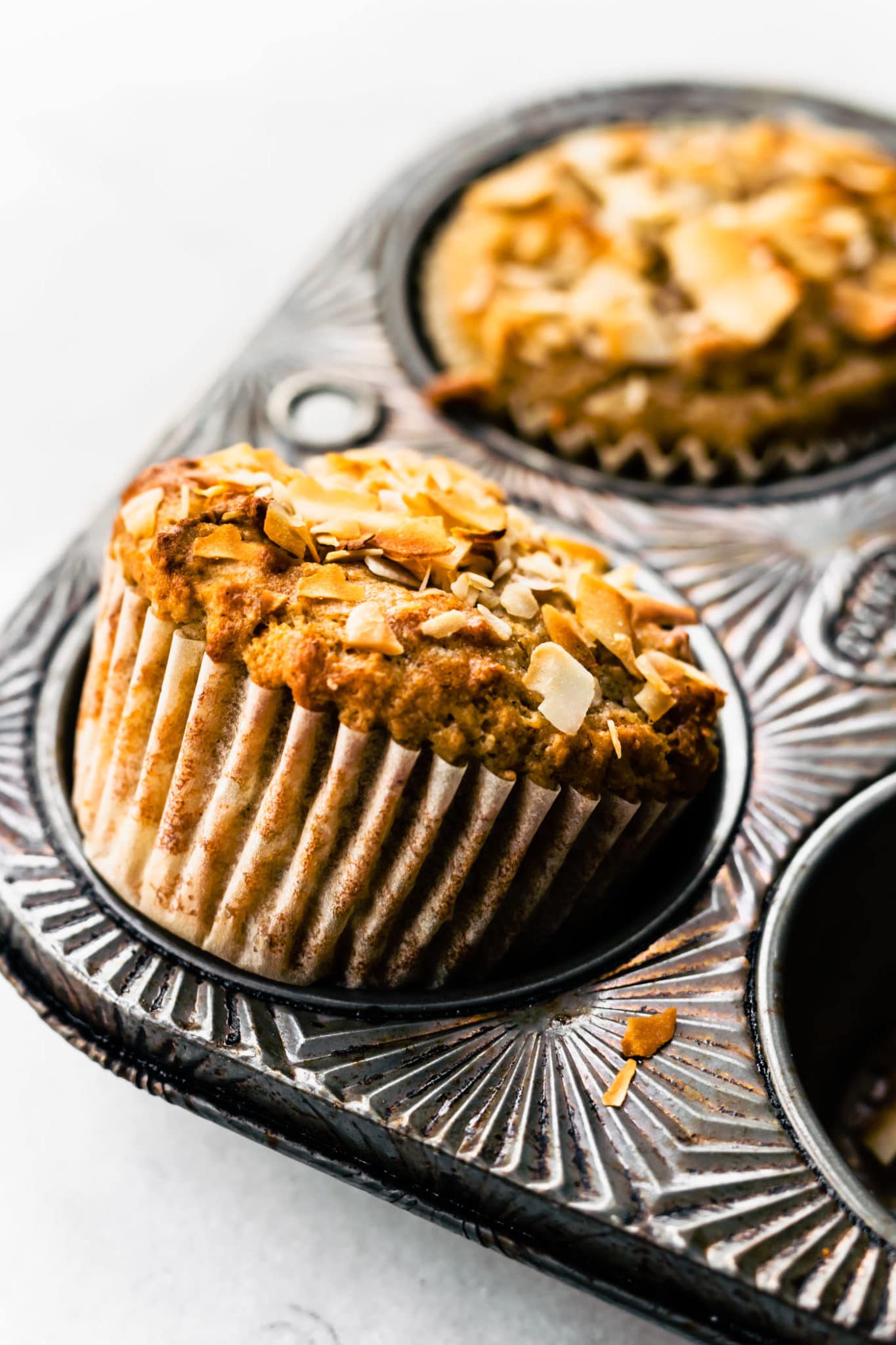 an almond flour banana muffin with coconut being popped out of a muffin tin