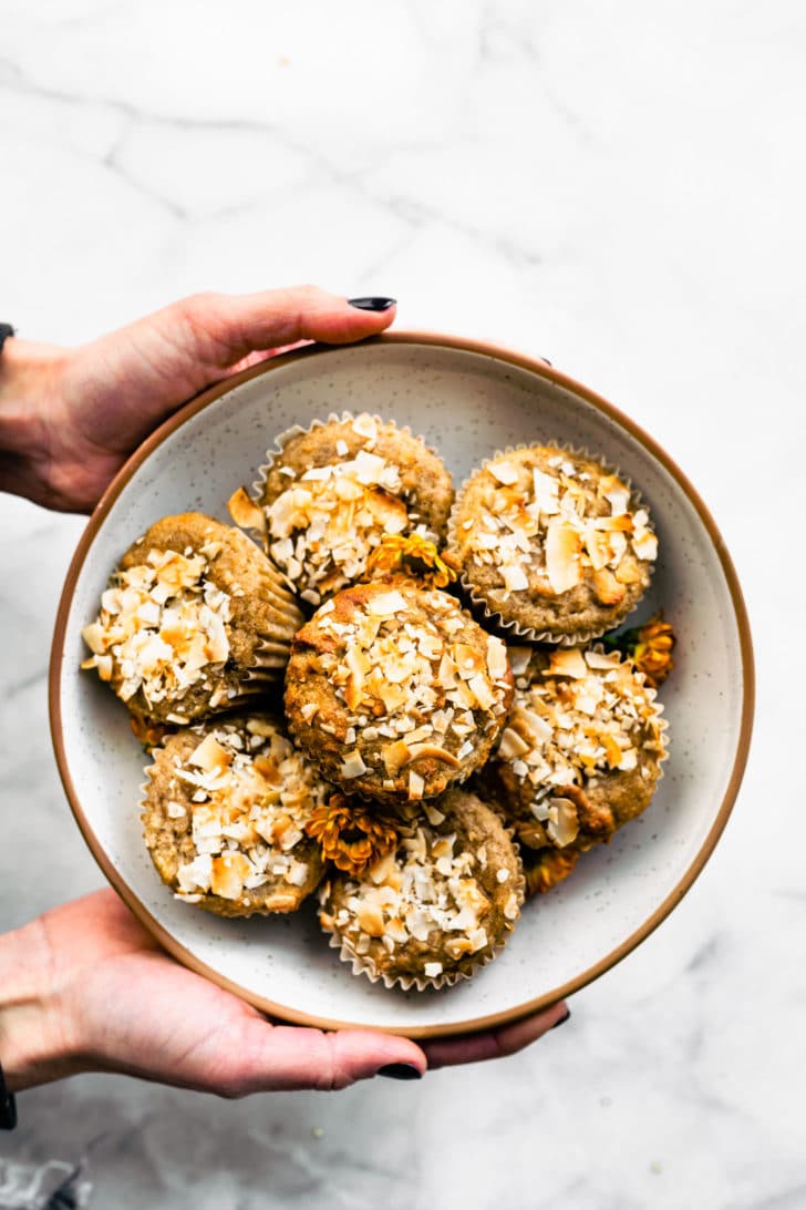two hands holding a plate with stacked almond flour banana muffins