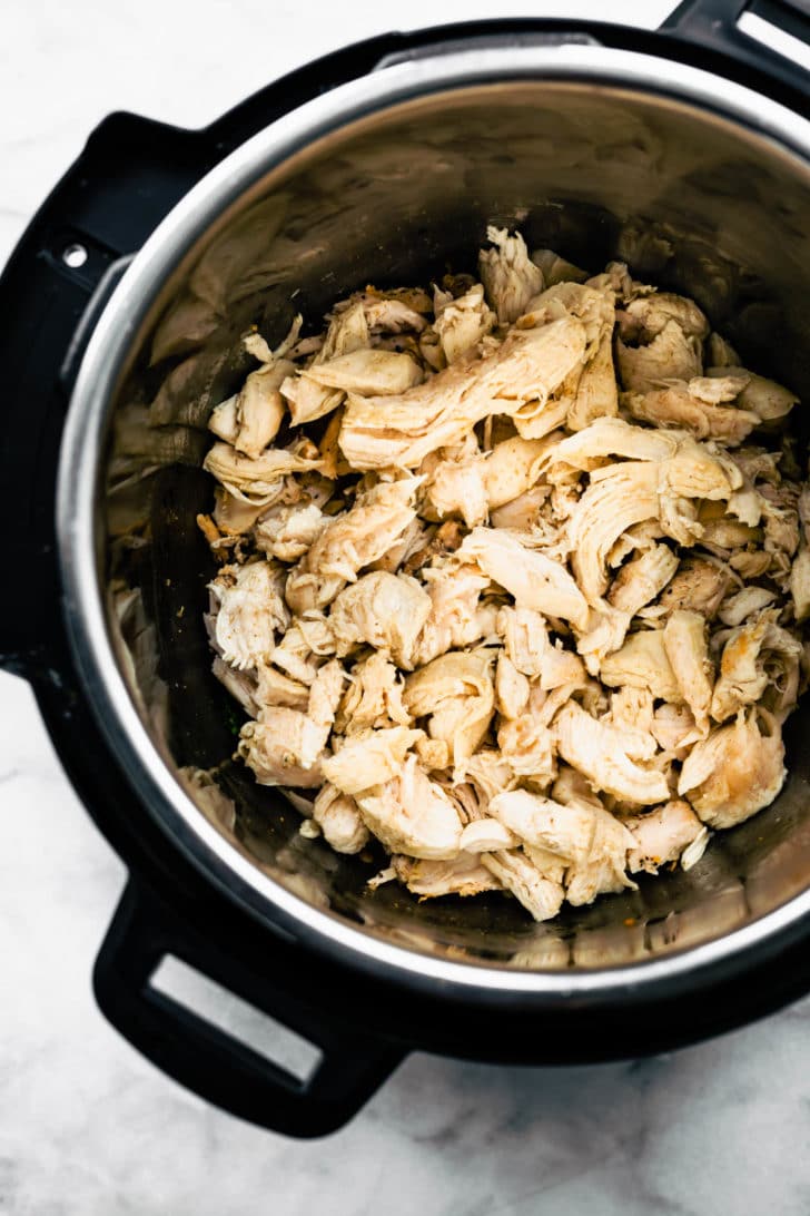 Overhead view of shredded chicken in an instant pot for chicken chili verde stew