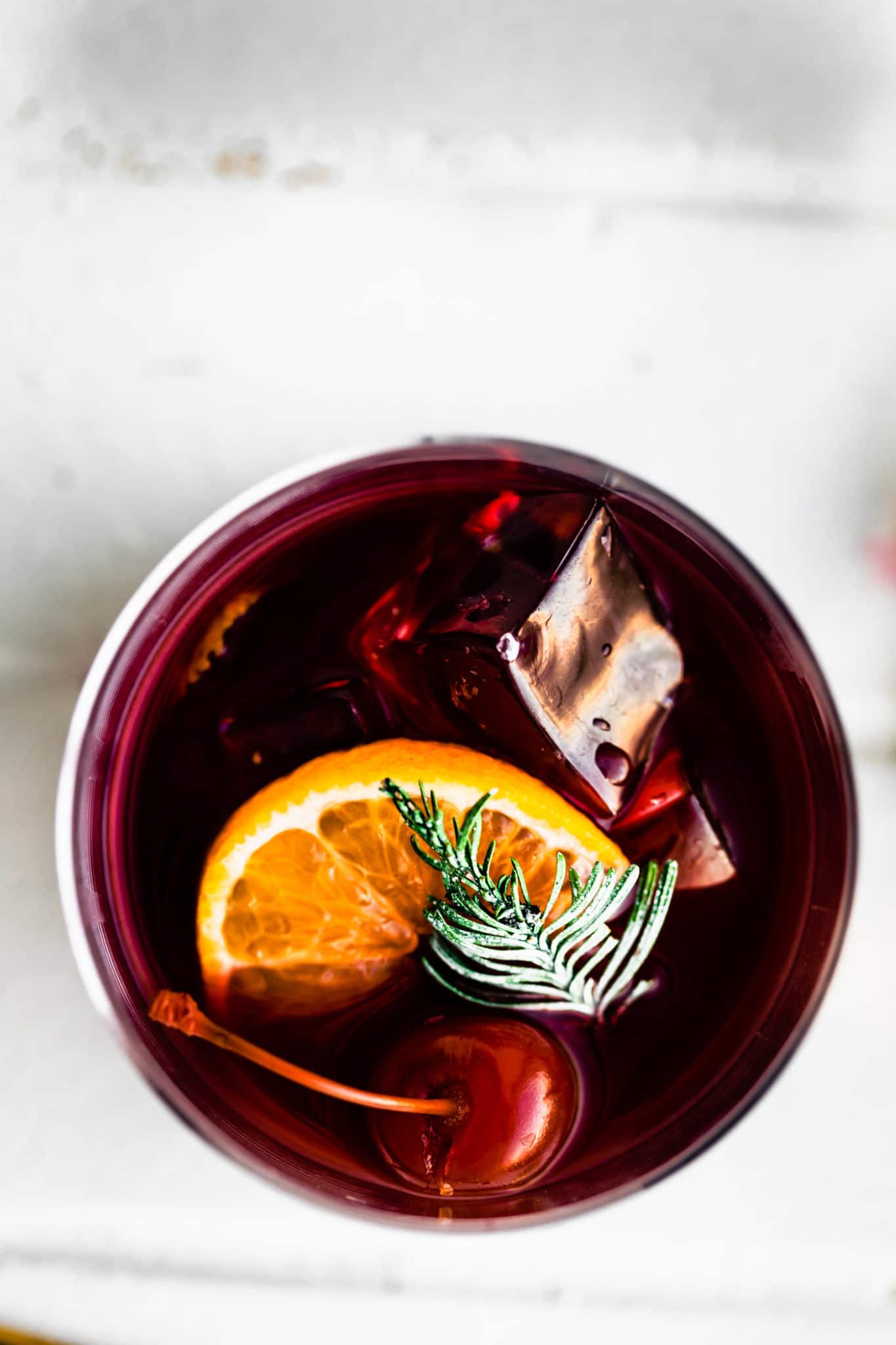 overhead image of a yuletide moon red wine cocktail garnished with an orange, cherries, and a sprig