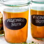 glass jars of homemade vegetable broth with "vegetable broth" written in white.