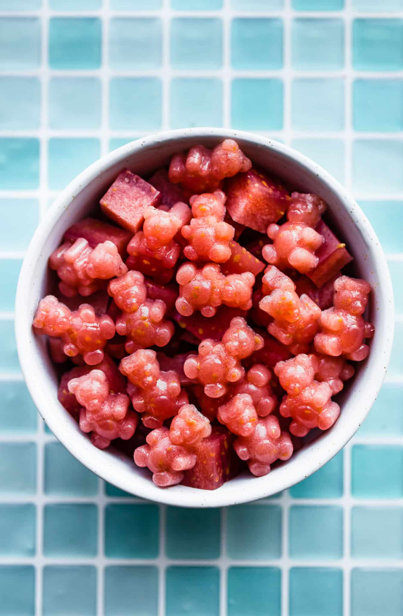 a white bowl filled with red homemade gummies with probiotics in the shape of cubes and bears