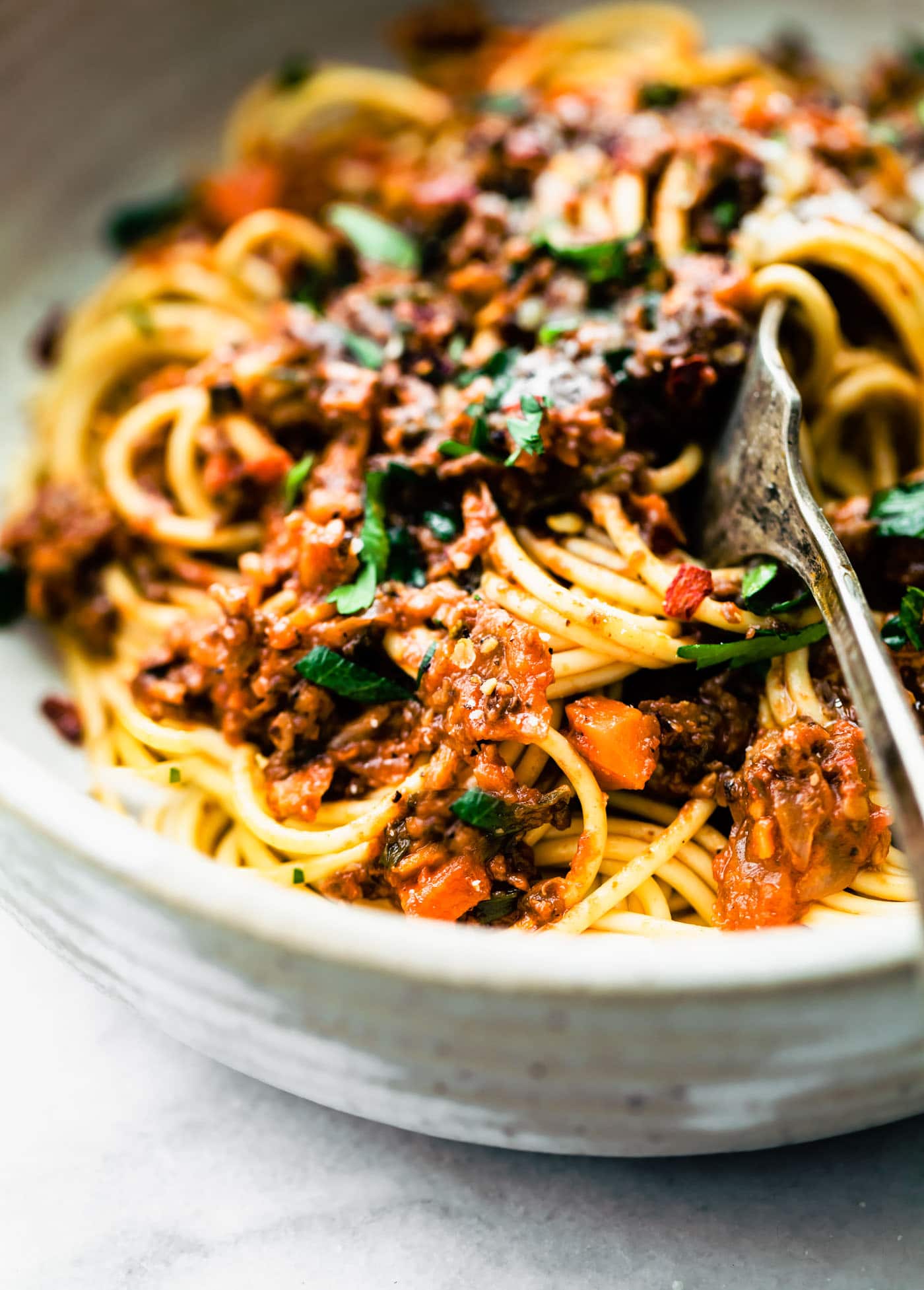 a close up image of gluten-free long pasta noodles topped with vegan bolognese sauce with a fork