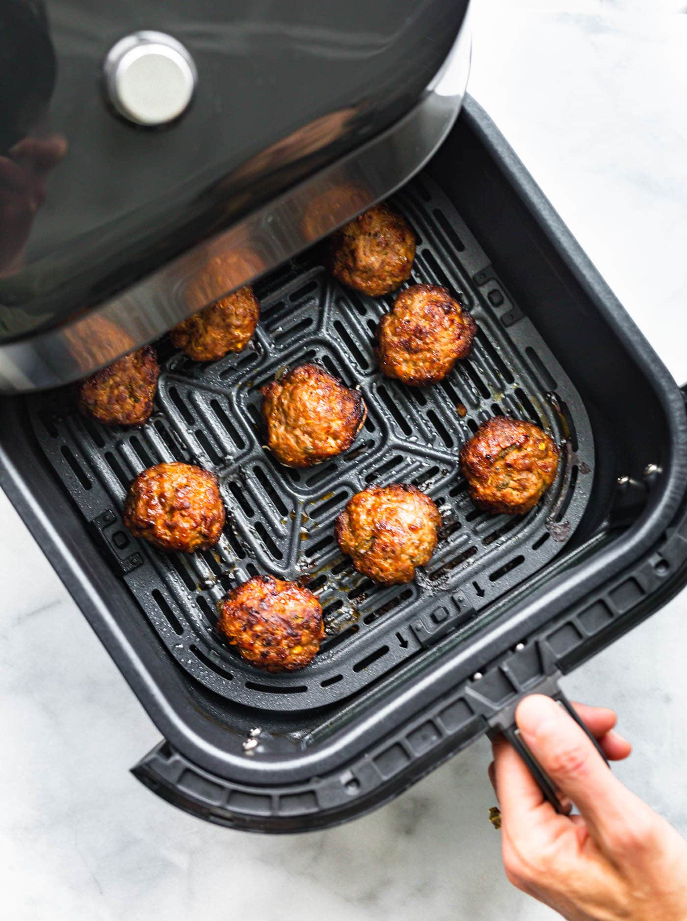 A hand pulling out an air fryer basket with cooked breakfast sausage patties
