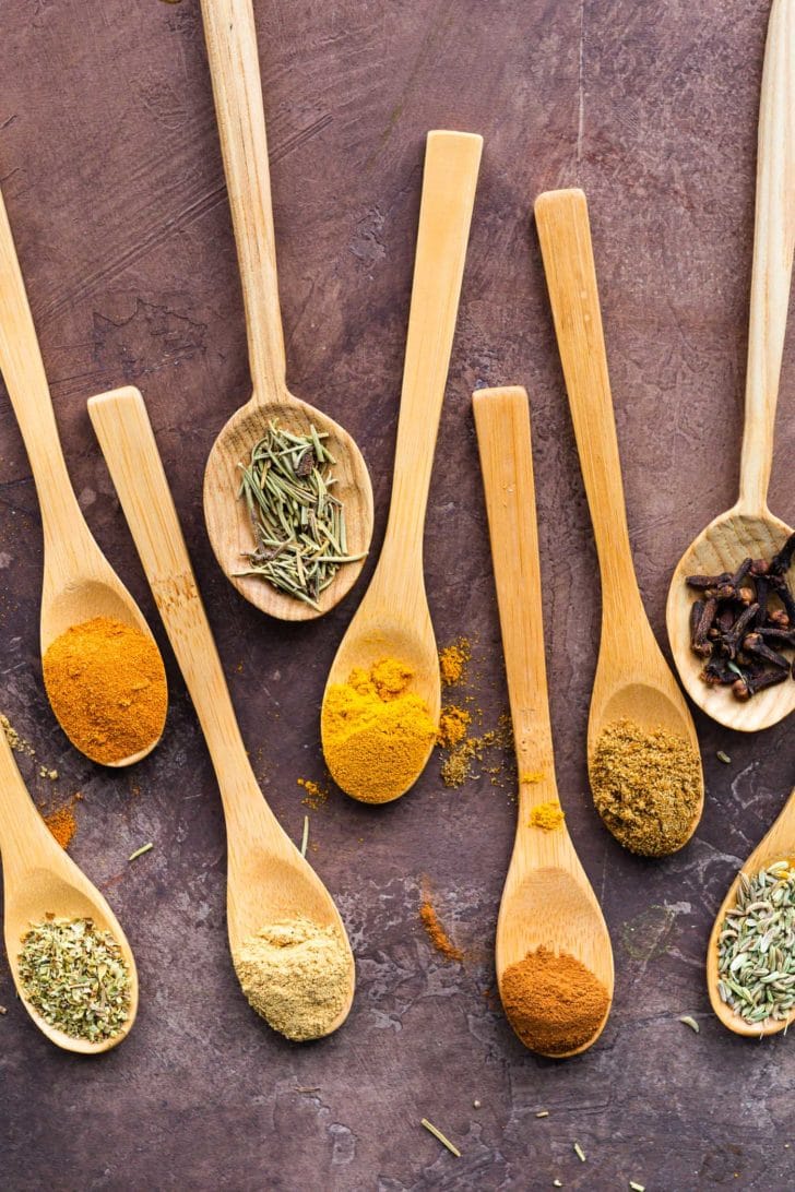 herbs and spices in wooden spoons with a dark background