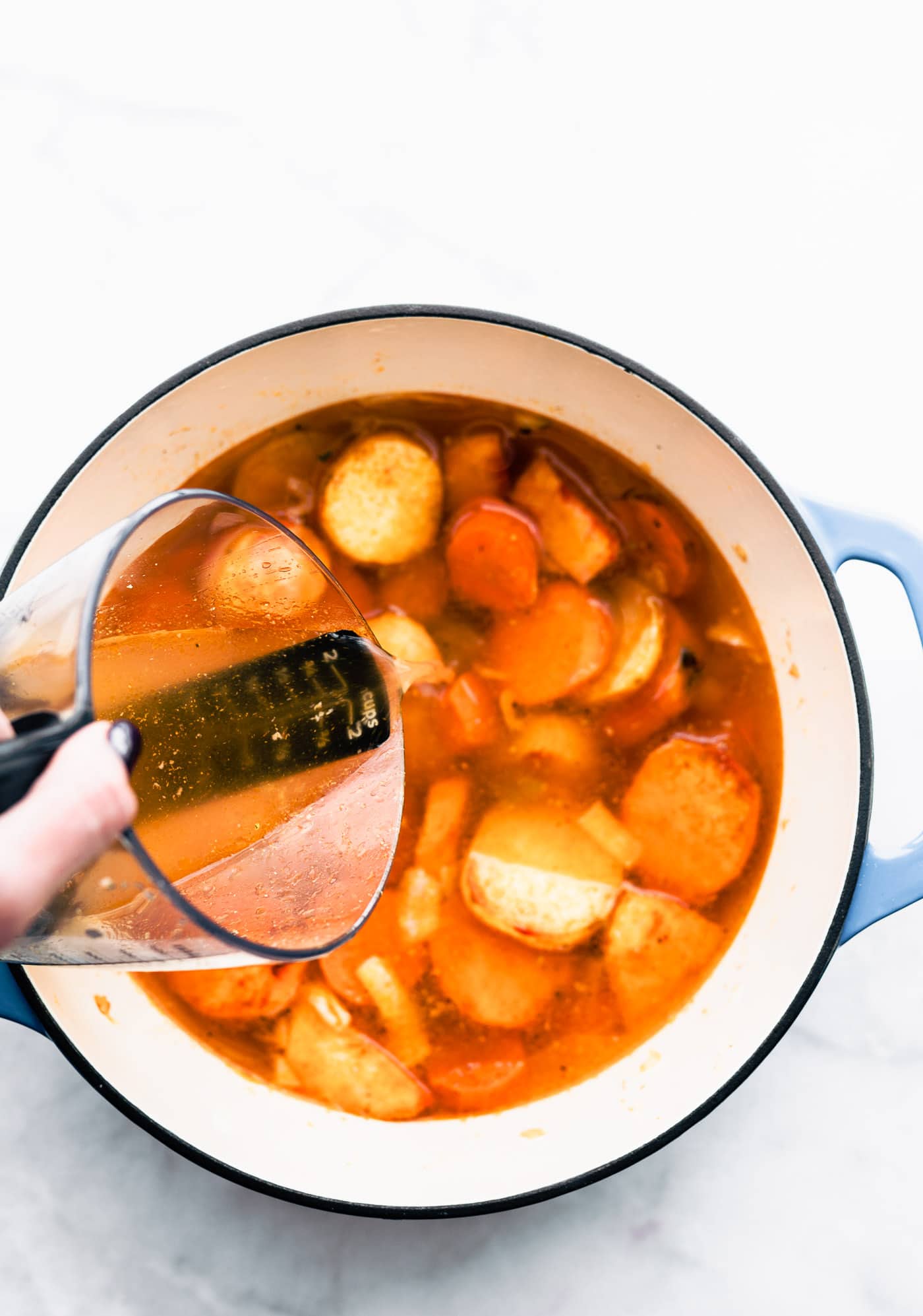 a pot of potatoes, parsnips, and carrots for root vegetable soup with a woman pouring broth into it