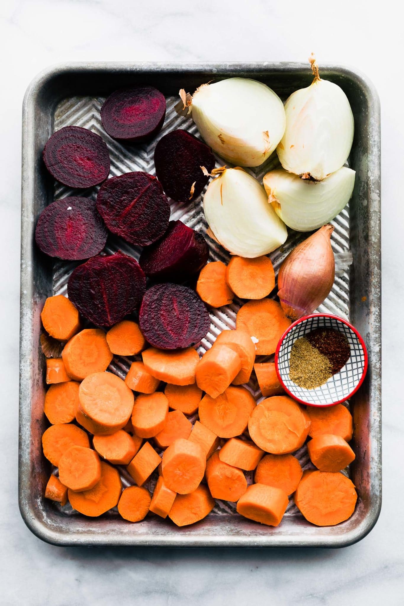 tray of sliced beets and carrots, overhead shot, with spices in bowl next to it.