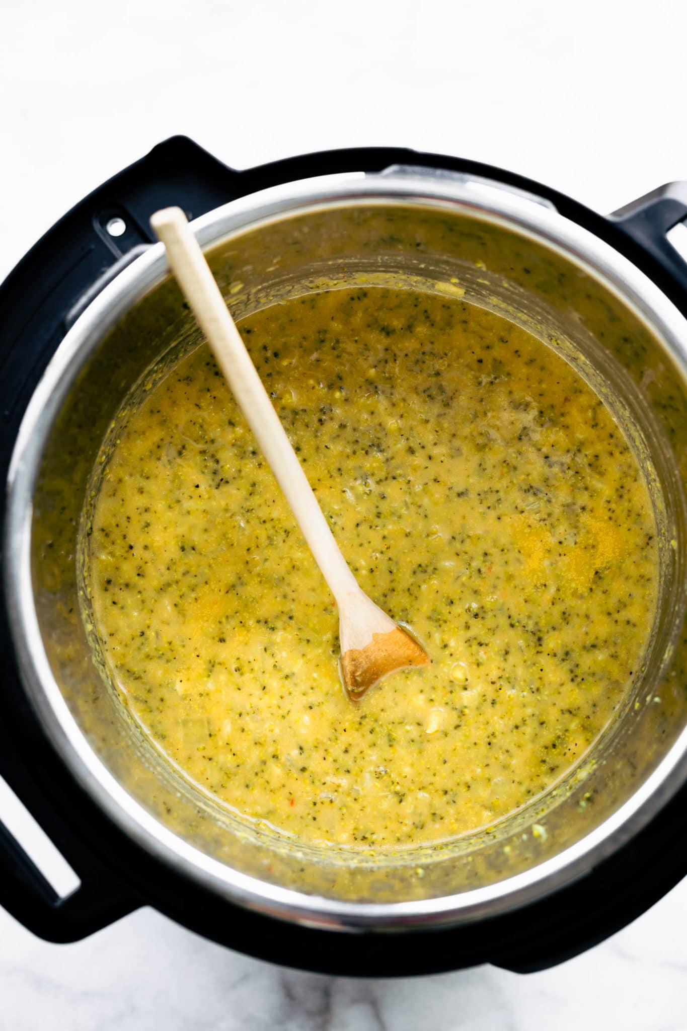 overhead image of vegan broccoli cheese soup in an instant pot with a wooden spoon