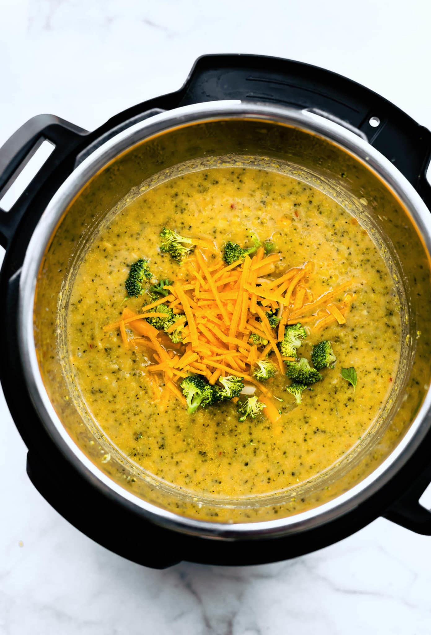 overhead image of vegan broccoli cheese soup in an instant pot topped with shredded dairy-free cheese