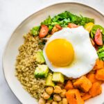 overhead image of a savory quinoa breakfast bowl with quinoa, chickpeas, sweet potatoes, spinach, tomatoes, avocado, and a fried egg