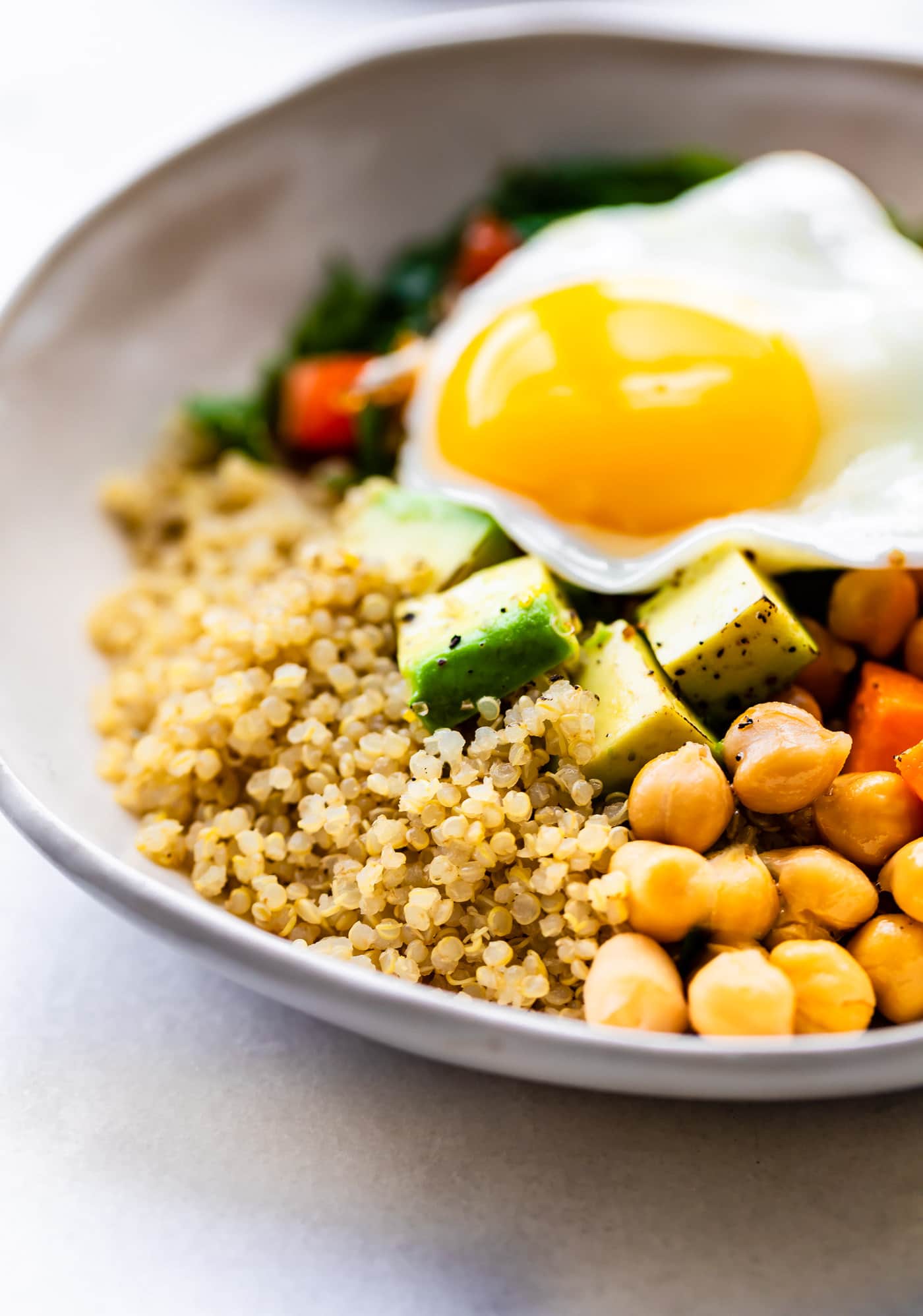 a savory quinoa breakfast bowl with quinoa, chickpeas, sweet potatoes, avocado, and a fried egg