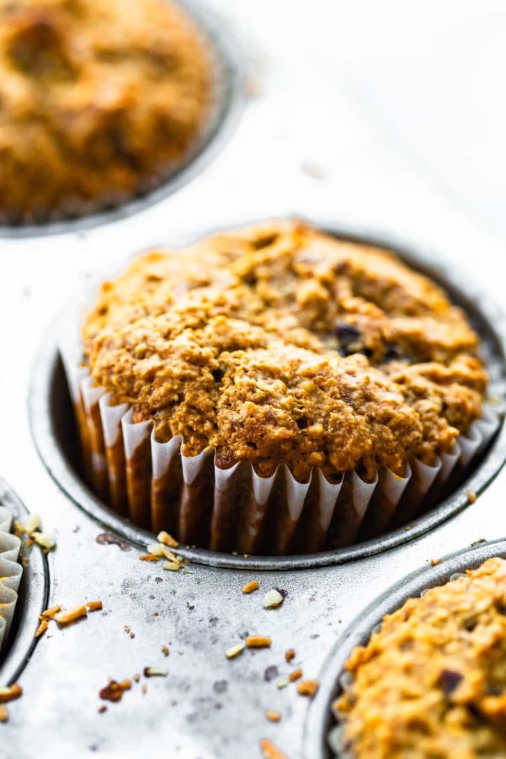 Close up photo of a gluten free carrot cake muffin popping out of the pan.