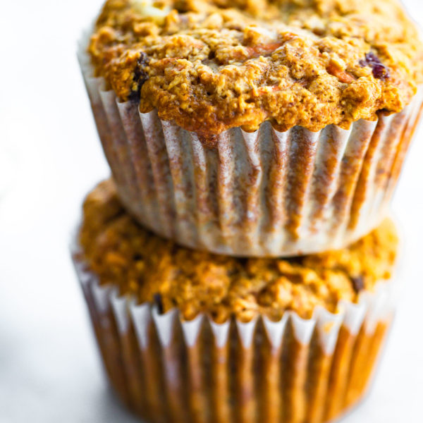 two healthy carrot cake muffins in muffin liners stacked on top of each other