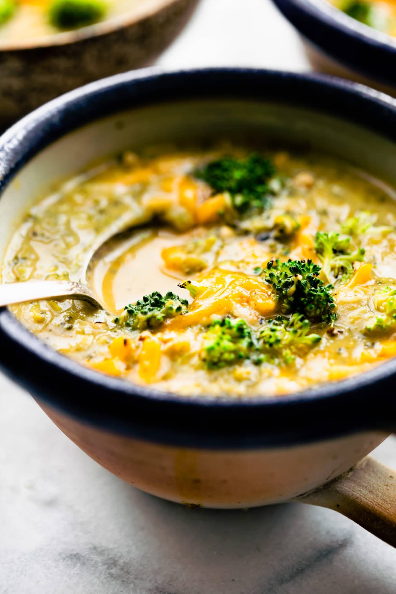 vegan broccoli cheese soup in a bowl topped with dairy-free cheese with a spoon dipping in